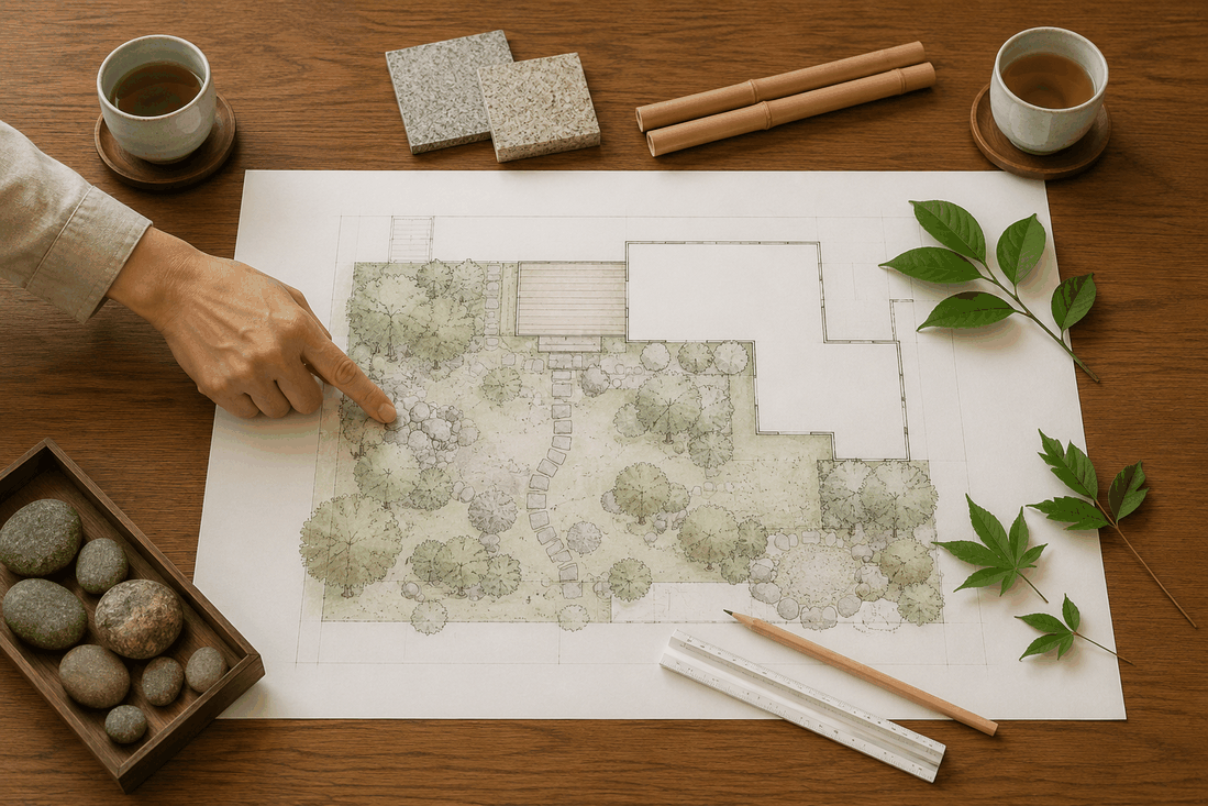 木の机に広げた庭の平面図と、図面を指す手、竹と石のサンプル